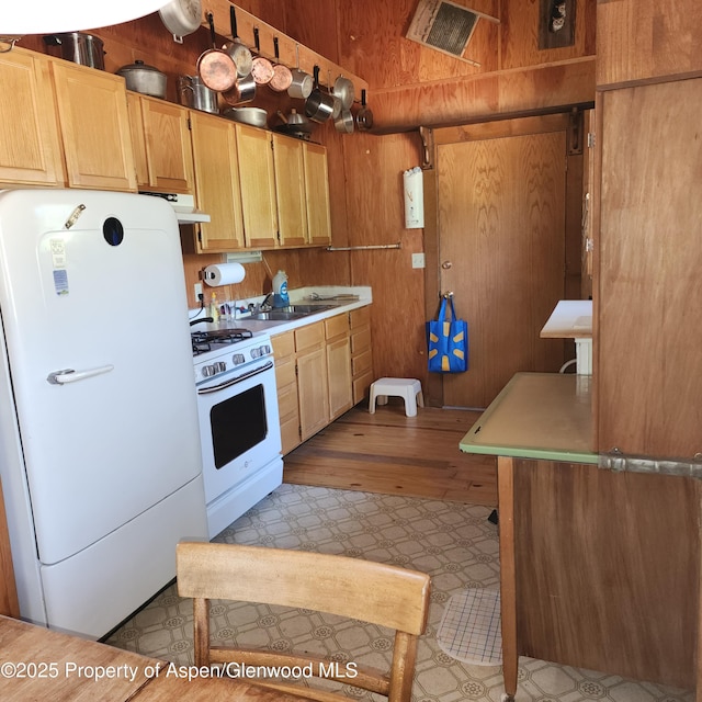 kitchen with white appliances, under cabinet range hood, a sink, and light countertops