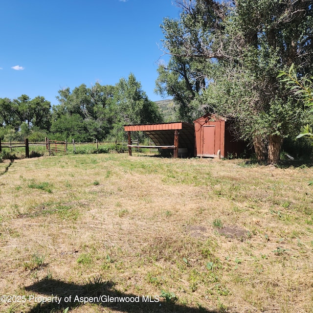 view of yard with an outdoor structure, a rural view, fence, and a shed