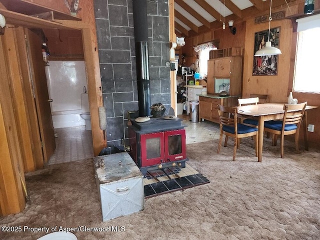 dining room featuring carpet flooring, lofted ceiling with beams, plenty of natural light, and a wood stove