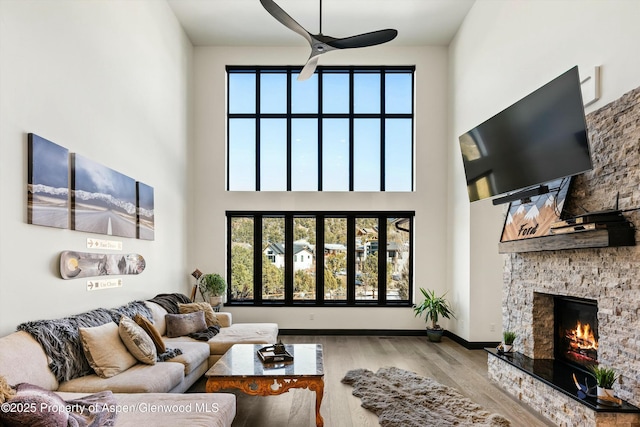 living room featuring a towering ceiling, a fireplace, ceiling fan, and light wood-type flooring