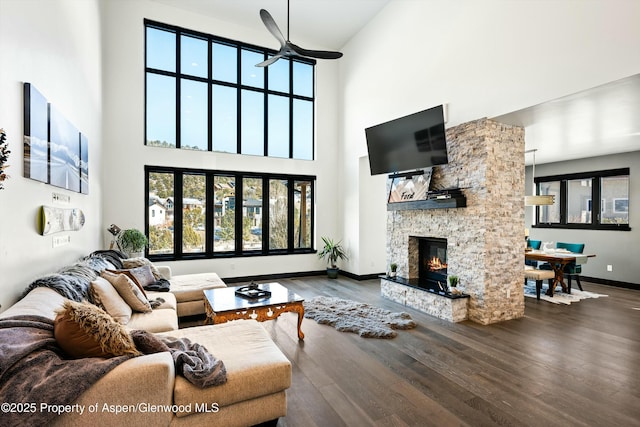 living room with ceiling fan, a stone fireplace, hardwood / wood-style floors, and a towering ceiling