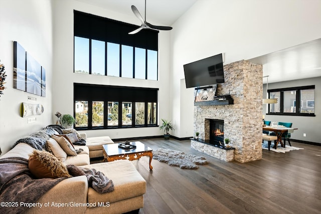 living room with hardwood / wood-style flooring, a stone fireplace, a towering ceiling, and ceiling fan