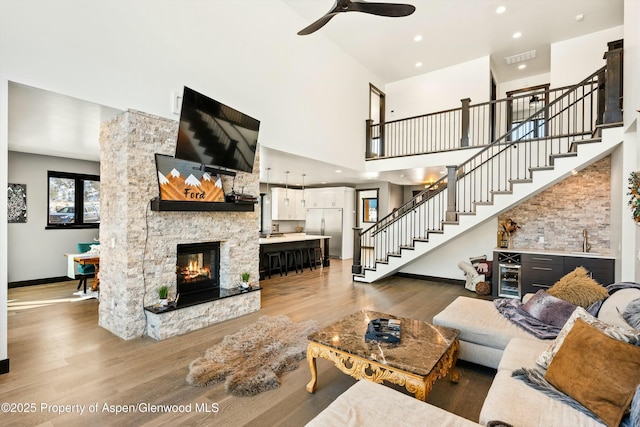 living room featuring ceiling fan, a stone fireplace, a high ceiling, and light wood-type flooring