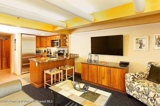 interior space featuring a kitchen bar, appliances with stainless steel finishes, dark stone countertops, kitchen peninsula, and backsplash