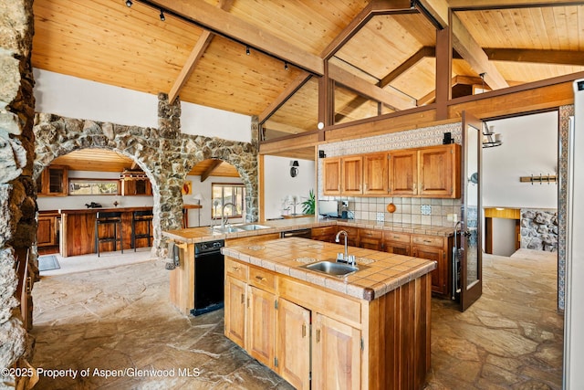 14 Fender Ln, Carbondale, CO 81623 - kitchen with a wood ceiling with exposed beams, stone flooring, a kitchen island with sink, tile counters, and arched walkways