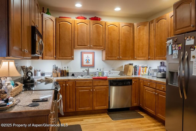 kitchen with a sink, light countertops, appliances with stainless steel finishes, light wood-type flooring, and brown cabinets