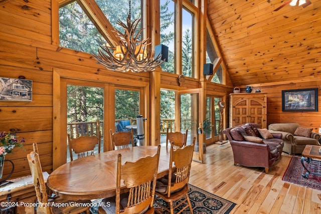 dining room with wood walls, light hardwood / wood-style floors, high vaulted ceiling, and french doors