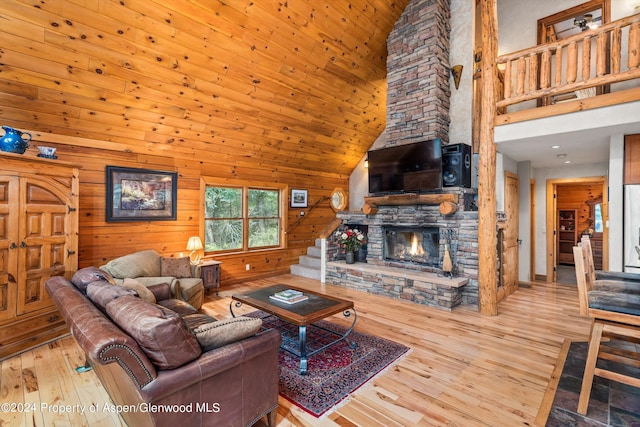 living room with wooden walls, a fireplace, high vaulted ceiling, and light hardwood / wood-style floors