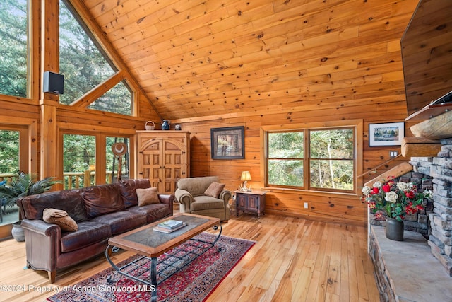 living room with a stone fireplace, wooden walls, high vaulted ceiling, and light hardwood / wood-style floors