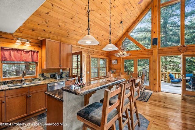 kitchen featuring sink, high vaulted ceiling, stainless steel dishwasher, dark stone counters, and decorative light fixtures