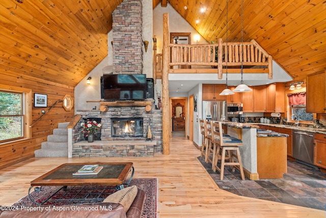 kitchen with stainless steel appliances, wooden walls, high vaulted ceiling, hanging light fixtures, and a breakfast bar area