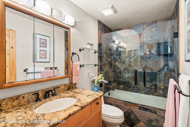 full bathroom featuring vanity, toilet, shower / bath combination with glass door, and a textured ceiling