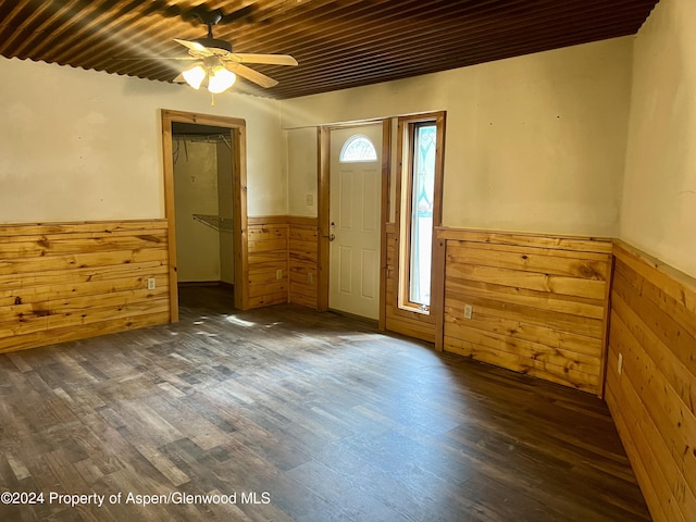 empty room with ceiling fan, wooden ceiling, dark wood-type flooring, and wooden walls