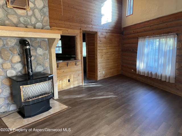 unfurnished living room with a wood stove, wood walls, a towering ceiling, and a healthy amount of sunlight