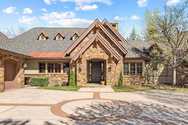 view of front of house with roof with shingles, a chimney, and stone siding