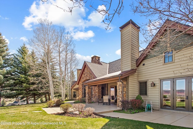 rear view of property with french doors, stone siding, a yard, and a chimney