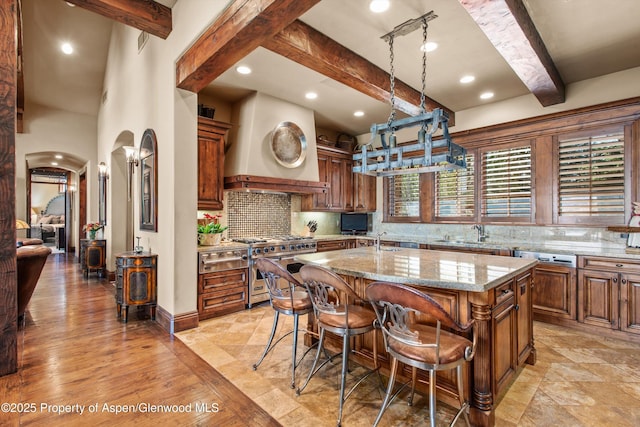 kitchen featuring designer stove, arched walkways, beam ceiling, and premium range hood