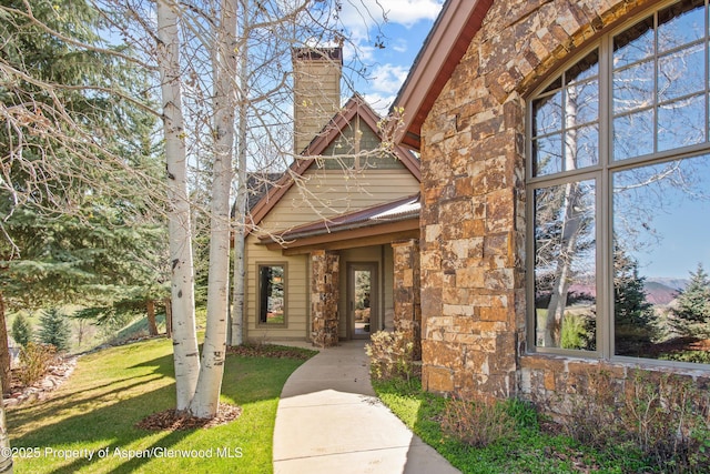 doorway to property featuring a chimney, a yard, and stone siding