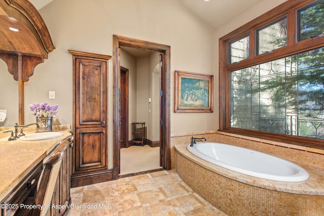bathroom with a bath, stone finish floor, lofted ceiling, and vanity