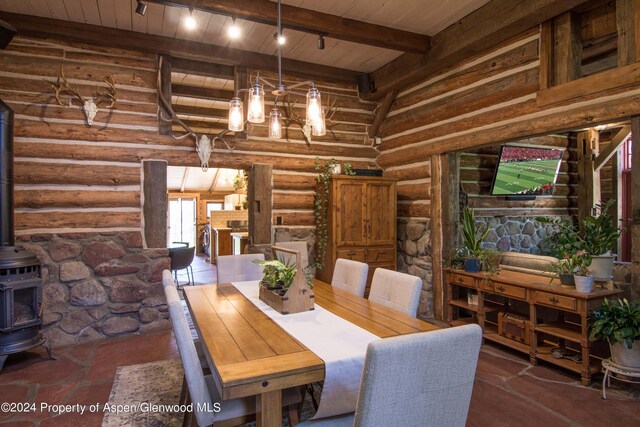 dining area featuring track lighting, rustic walls, wooden ceiling, beamed ceiling, and a wood stove