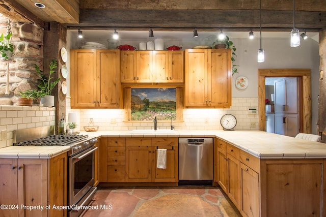 kitchen featuring pendant lighting, backsplash, appliances with stainless steel finishes, tile counters, and kitchen peninsula