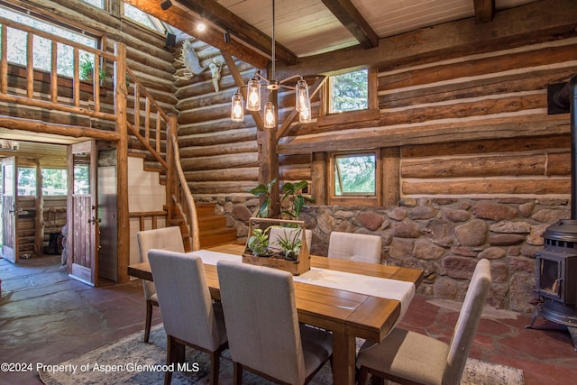 unfurnished dining area featuring rustic walls, a wood stove, a high ceiling, an inviting chandelier, and beamed ceiling