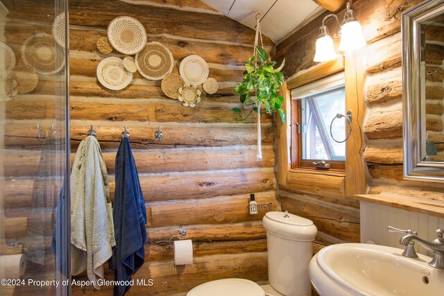 bathroom featuring toilet, lofted ceiling, sink, and log walls