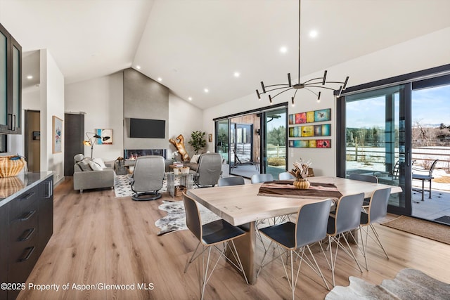 dining space with a notable chandelier, high vaulted ceiling, a fireplace, and light wood-style floors