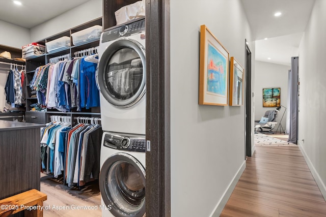 laundry room with stacked washer and dryer, wood finished floors, laundry area, and baseboards