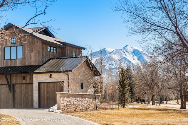 view of home's exterior with a standing seam roof, metal roof, a garage, stone siding, and driveway