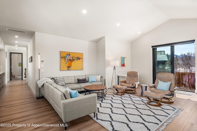 living room featuring baseboards, visible vents, vaulted ceiling, and wood finished floors