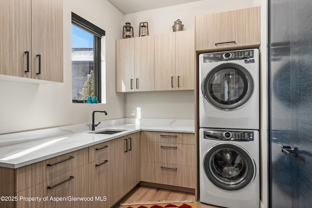 clothes washing area featuring stacked washer and dryer, light wood-type flooring, a sink, and cabinet space