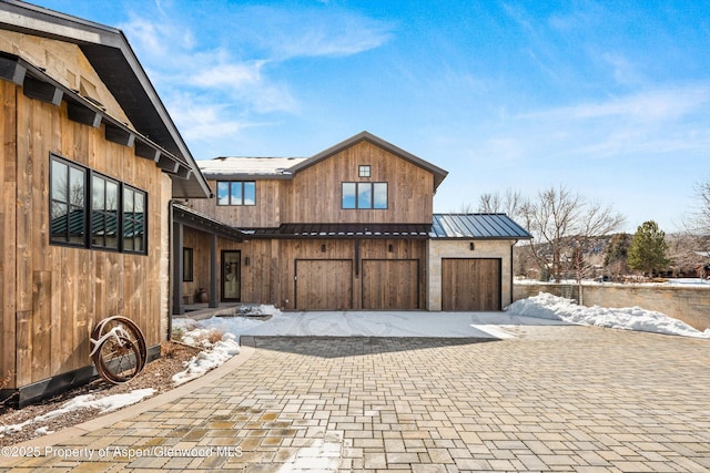 view of snowy exterior featuring decorative driveway, a standing seam roof, and metal roof