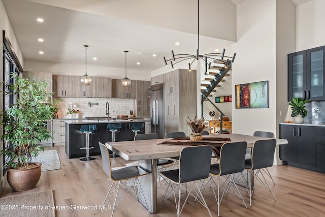 dining space with light wood-style floors, recessed lighting, stairway, and a high ceiling