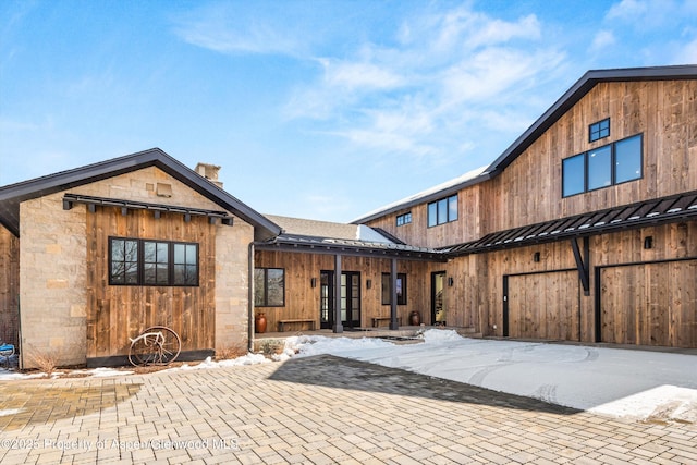 snow covered back of property with stone siding, a standing seam roof, and metal roof