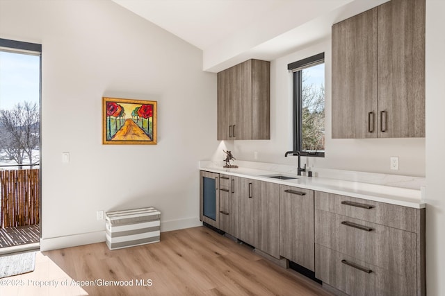 bar featuring light wood-style flooring, baseboards, and a sink