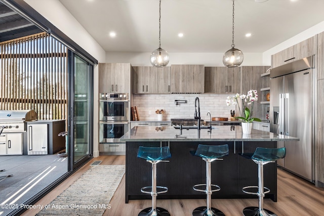 kitchen with a sink, modern cabinets, appliances with stainless steel finishes, and dark stone countertops