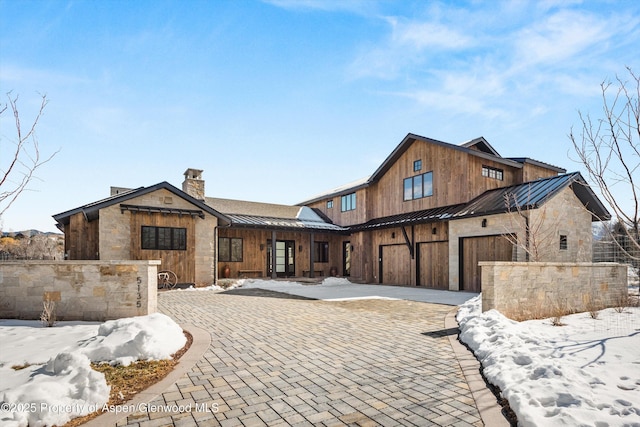 view of front of house with a standing seam roof, metal roof, an attached garage, stone siding, and a chimney