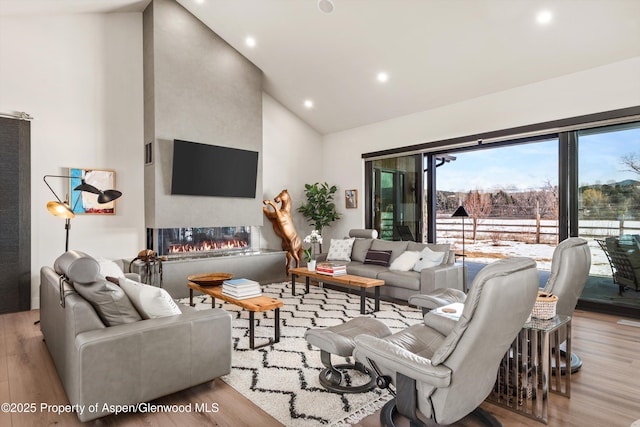 living area featuring high vaulted ceiling, recessed lighting, a multi sided fireplace, and wood finished floors