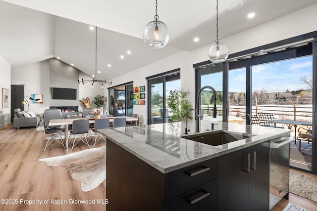 kitchen with light wood-style flooring, open floor plan, hanging light fixtures, a kitchen island with sink, and a sink