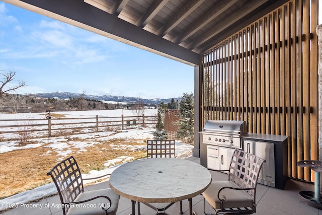 snow covered patio featuring outdoor dining space, area for grilling, fence, and a mountain view