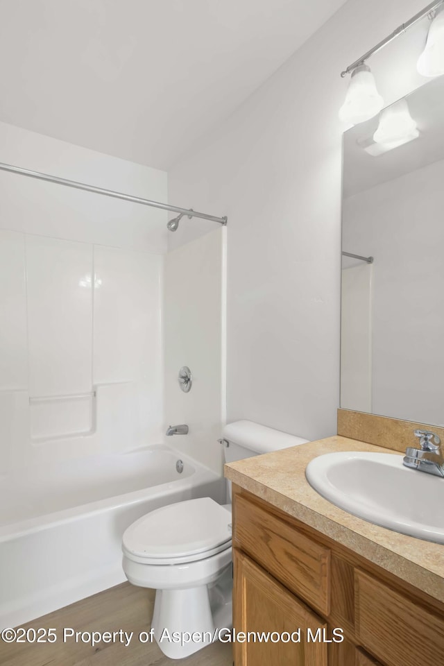 full bathroom with hardwood / wood-style flooring, vanity, washtub / shower combination, and toilet