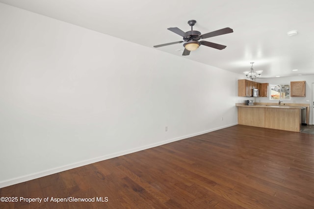 unfurnished living room featuring ceiling fan with notable chandelier and dark hardwood / wood-style floors