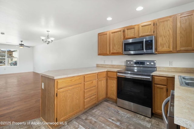 kitchen featuring sink, wood-type flooring, appliances with stainless steel finishes, kitchen peninsula, and ceiling fan with notable chandelier