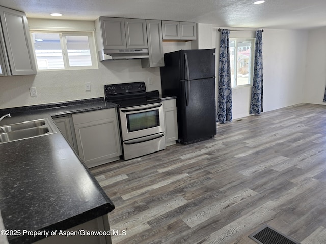 kitchen with sink, stainless steel range with electric cooktop, gray cabinetry, black fridge, and hardwood / wood-style floors