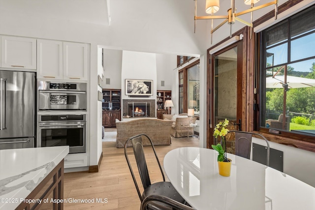 11 Pinon Ln, Carbondale, CO 81623 - dining area with light wood-style floors, a chandelier, a lit fireplace, and a high ceiling