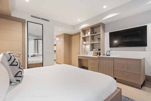 bedroom with sink, connected bathroom, and light hardwood / wood-style flooring