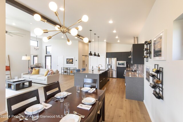 dining area featuring light hardwood / wood-style flooring, a towering ceiling, ceiling fan with notable chandelier, and sink