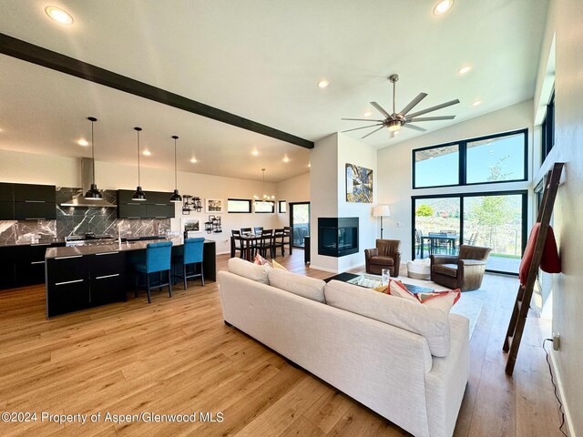 living room featuring high vaulted ceiling, ceiling fan with notable chandelier, and light wood-type flooring