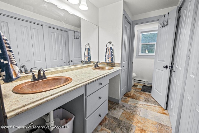 3598 County Road 35, Craig, CO 81625 - bathroom featuring stone tile floors, a baseboard radiator, toilet, double vanity, and a closet